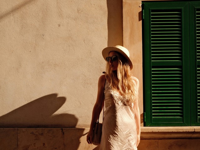A traveler in a sun hat standing beside green shutters